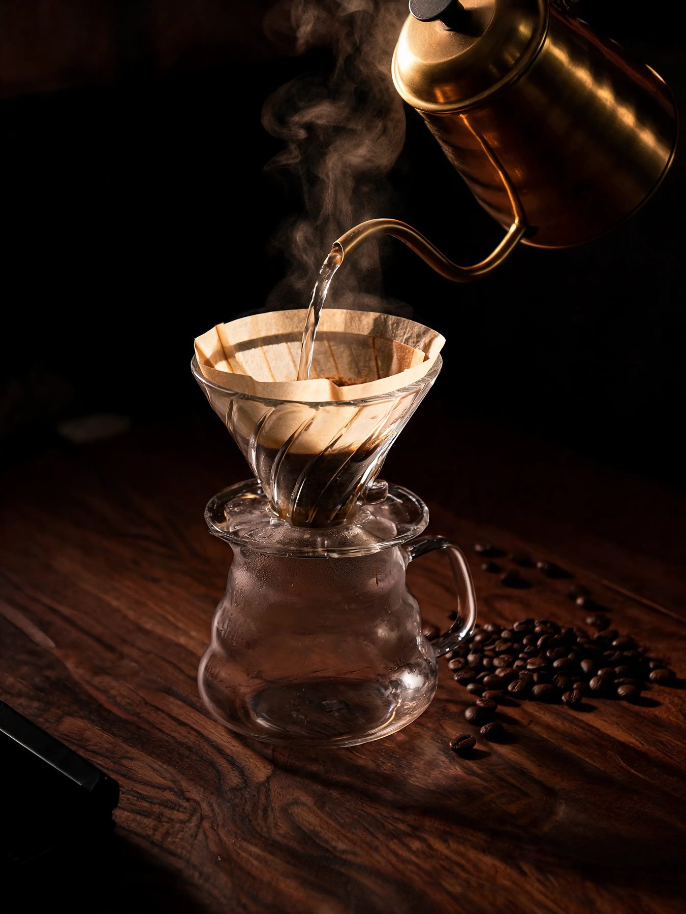 Gooseneck kettle pouring into a glass dripper on a dark walnut counter